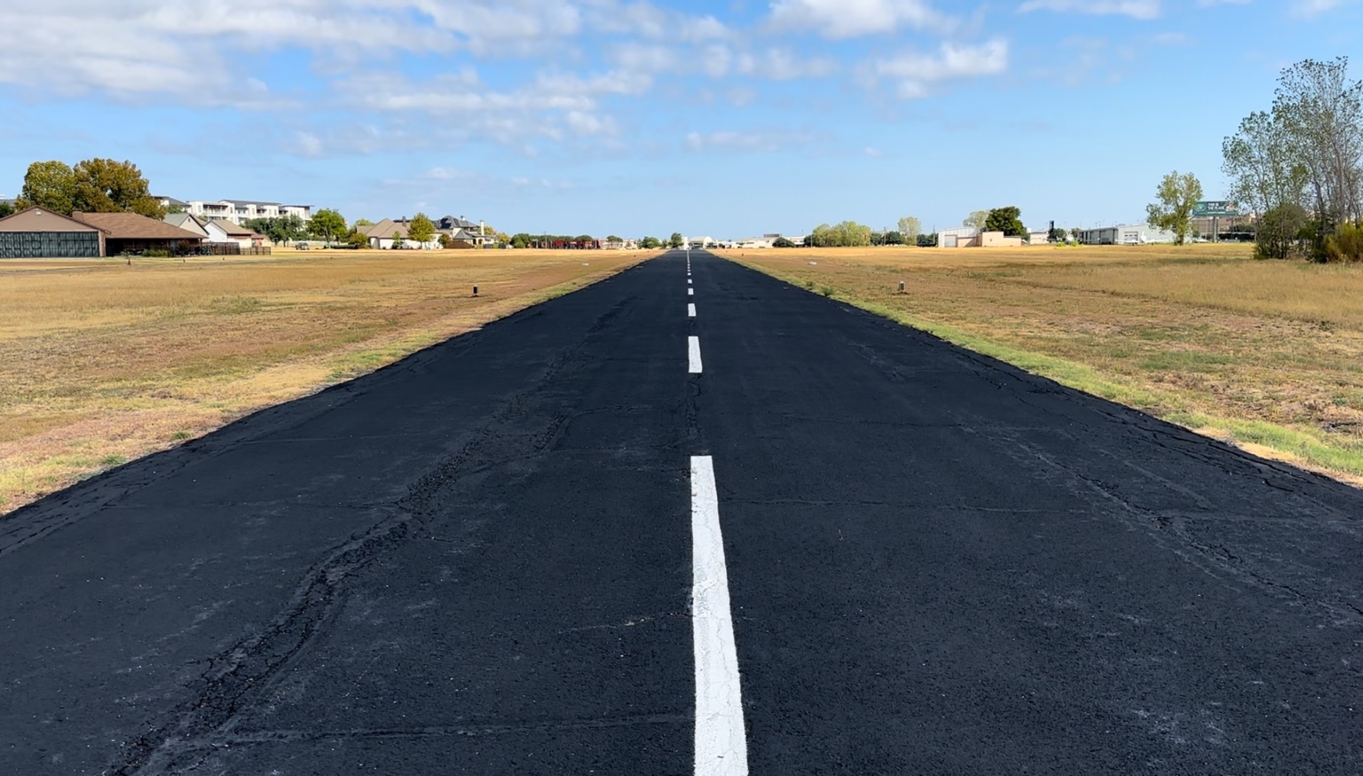 Ground-level view down the centerline at Air Park Dallas with homes and hangars nearby