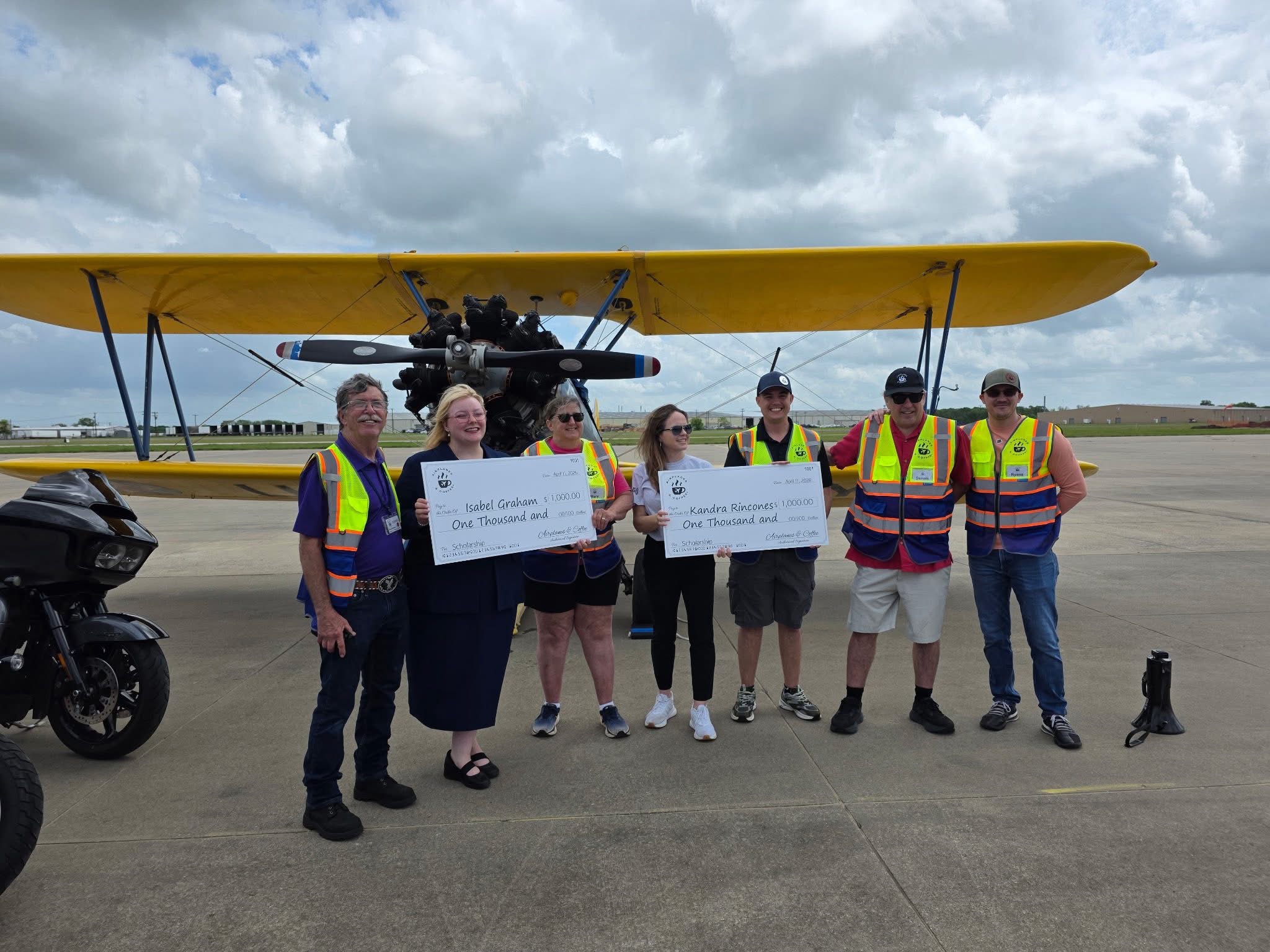 Airplanes and Coffee volunteers presenting aviation scholarships in front of a yellow biplane