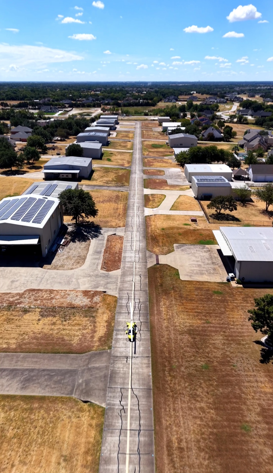 Yellow gyrocopter taxiing on a concrete taxiway lined by private hangars at Eagle’s Nest Estates