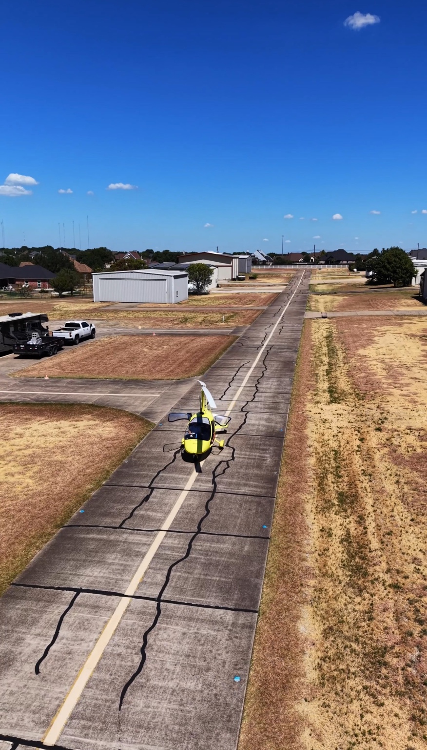Yellow gyrocopter on a concrete taxiway lined by private hangars at Eagle’s Nest Estates