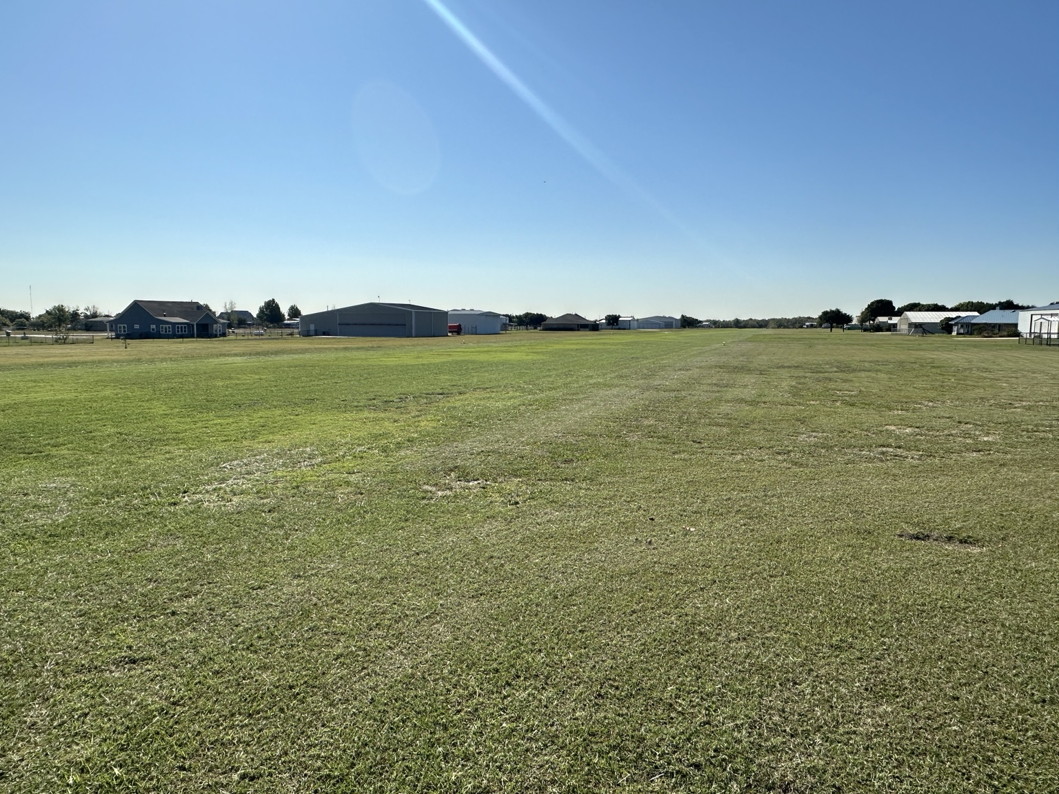 Wide ground-level view across Fairview Airport’s turf runway and surrounding properties