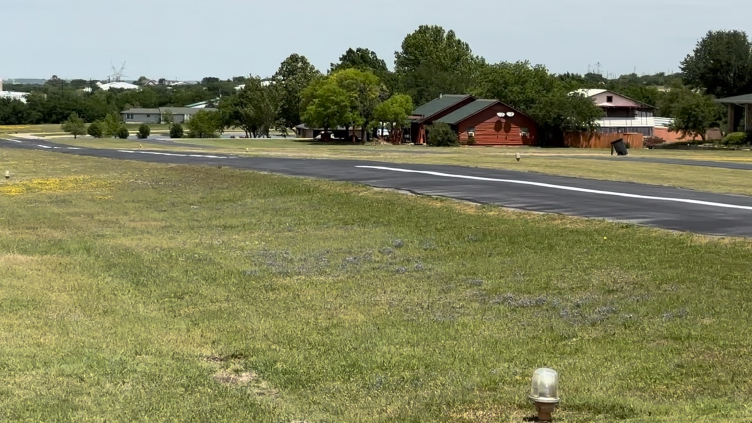 Ground view of the paved runway with homes and hangars at Hillcrest Airport