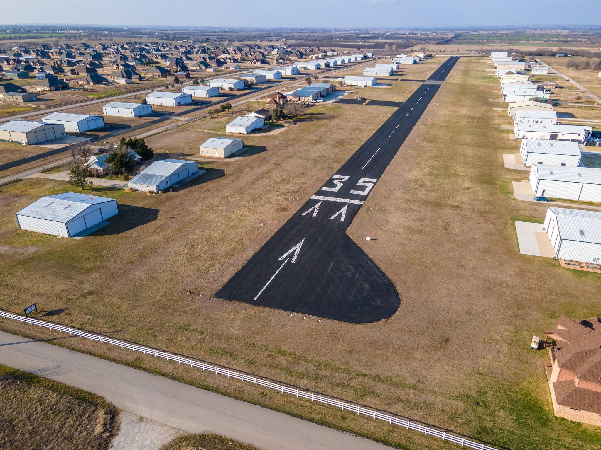 Aerial view down Runway 17/35 at Propwash Airport (16X) with hangars and homes
